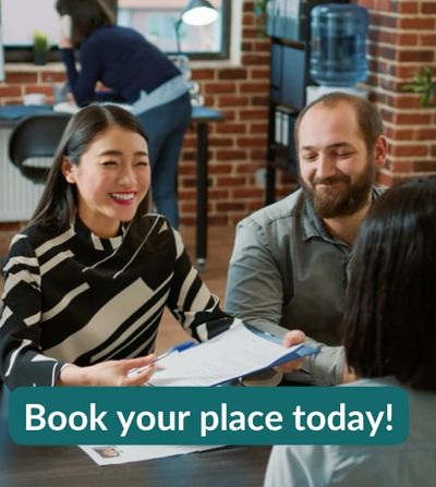 Group of people smiling at a meeting around a desk. Main person is making reference to a document. 