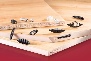 Wooden boards with various black and silver furniture connectors on a red surface.