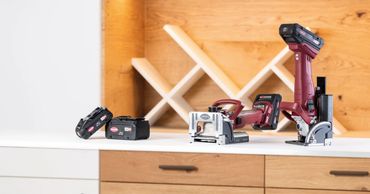 Cordless power tools displayed on a kitchen countertop with wooden cabinets.