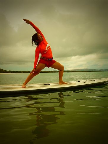 Woman performing yoga pose on paddleboard on calm water at sunset.