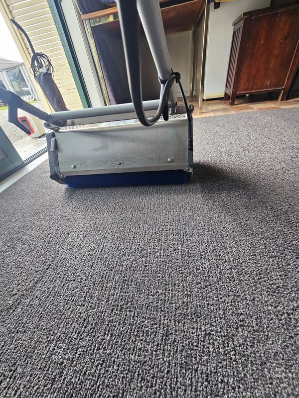 A carpet cleaning machine on a textured gray carpet indoors.