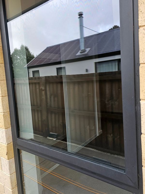 A closed window reflecting a house and wooden fence outside.