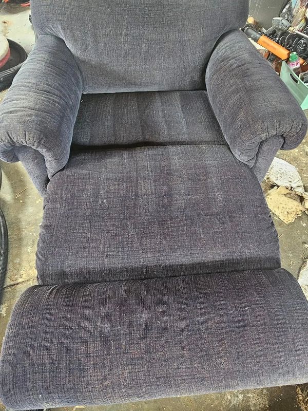 A well-used, dark gray recliner chair with visible wear.