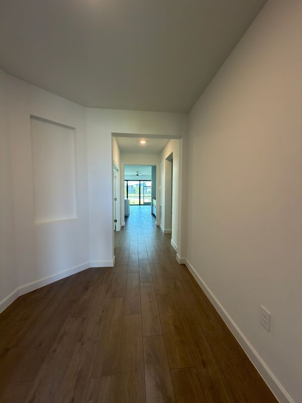 Empty hallway with wooden flooring leading to a bright living area.