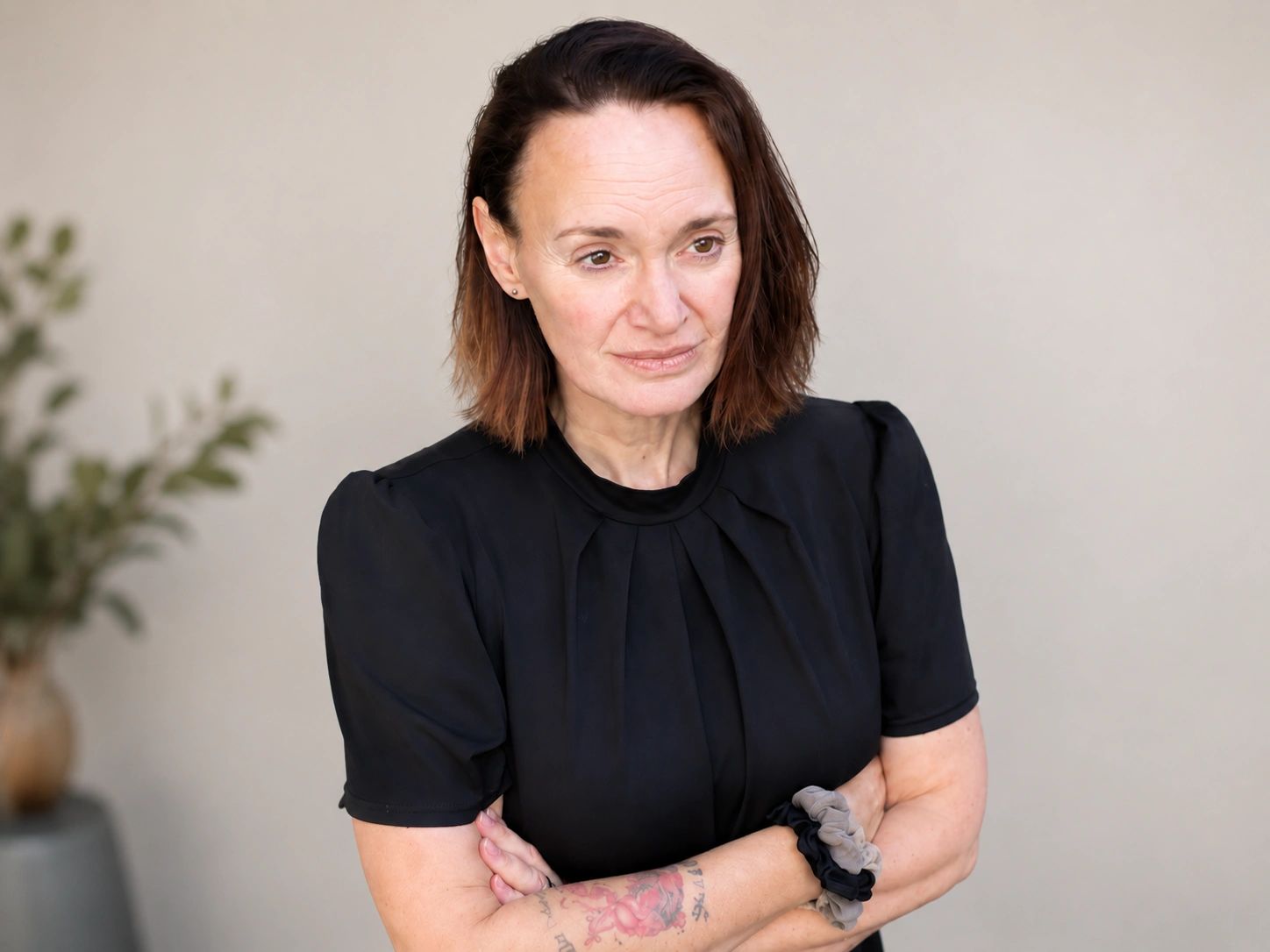 Woman in black top with tattoo and scrunchies looking thoughtful.