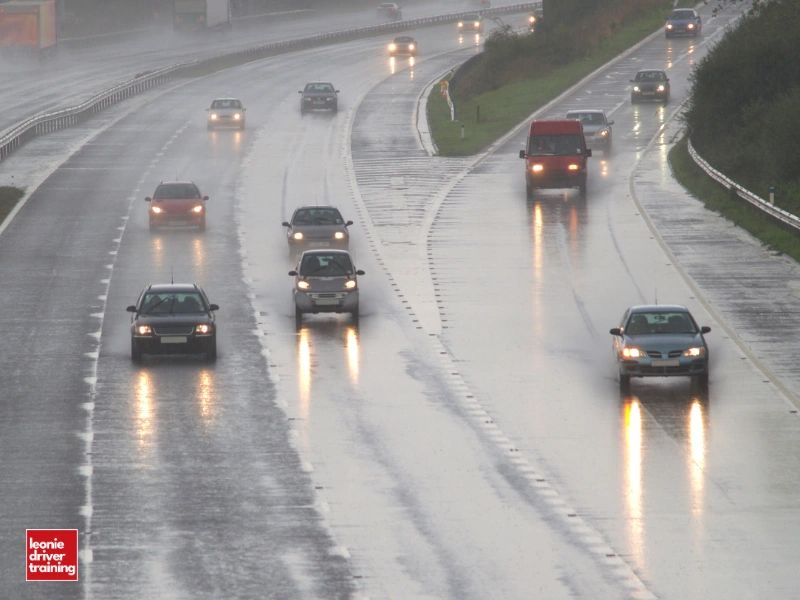 Cars driving on a wet, rainy highway with headlights on.
