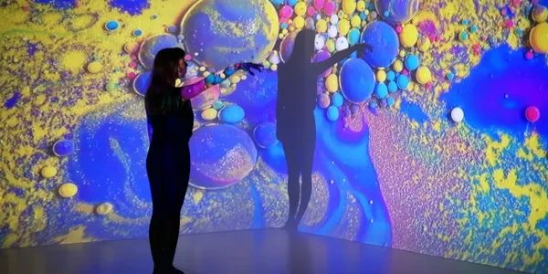 A person interacts with an immersive, colorful art projection of bubbles and abstract forms.