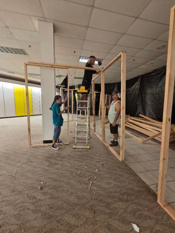 Three people constructing a wooden frame indoors.