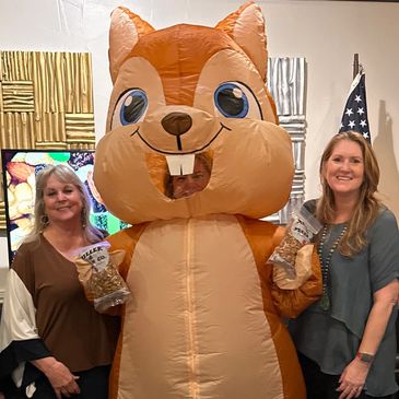 Two women and a large squirrel mascot holding bags of snacks.