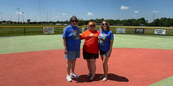 Three women standing on a baseball field on a sunny day.