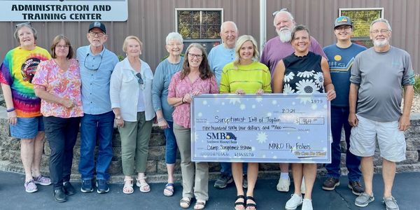Group holding a large donation check outside a building.