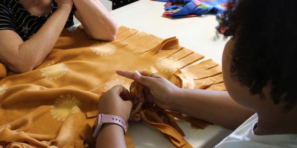 People tying knots on a fleece blanket together.