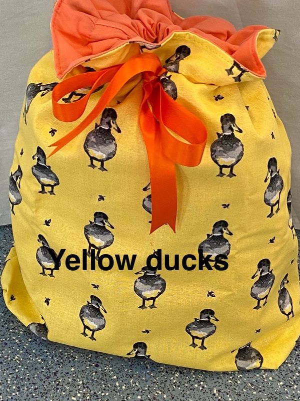 A reusable fabric gift bag in yellow fabric with grey ducks. Finished with an orange ribbon tie