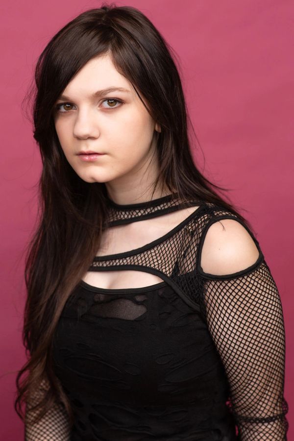 Young woman with long dark hair in a black fishnet top against a pink background.