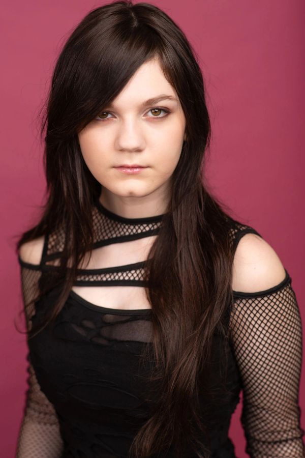 Young woman with long dark hair in black mesh outfit against pink background.