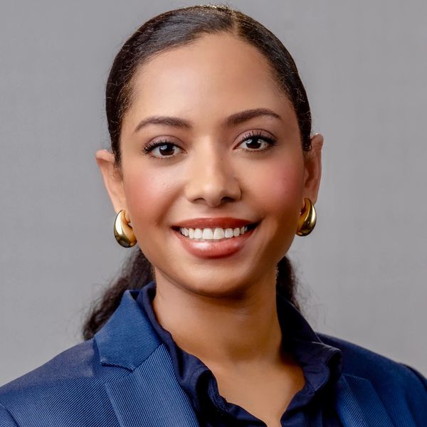 Professional woman smiling, wearing a blue blazer and gold earrings.