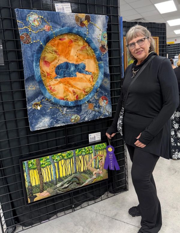 Woman posing with award-winning artwork at exhibition.