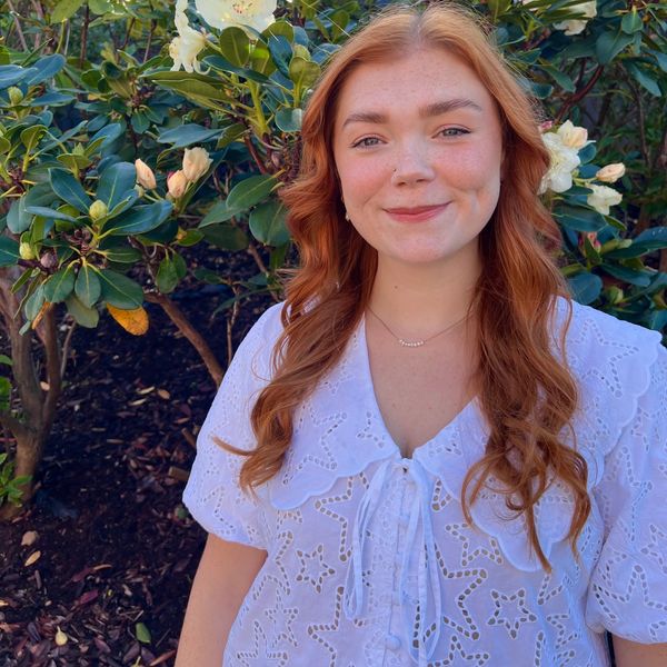 Smiling woman with red hair in white blouse outdoors.