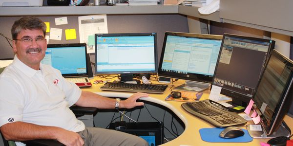 Man smiling at desk with multiple computer screens.