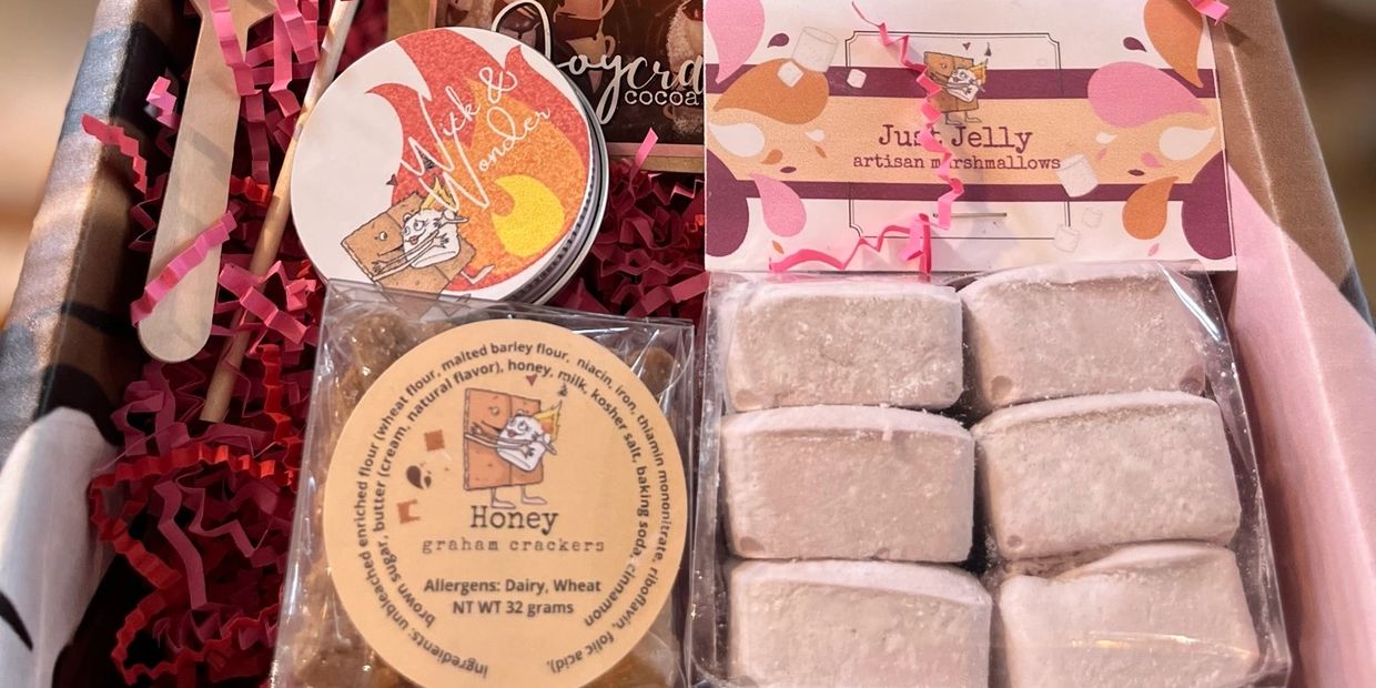 Box that include artisan marshmallows, honey graham crackers, a candle, and pink crinkle paper