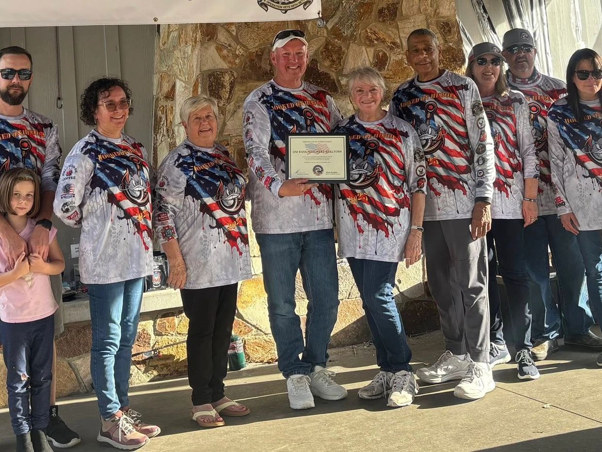 Group of people wearing matching patriotic shirts, one holding a certificate, standing outdoors.