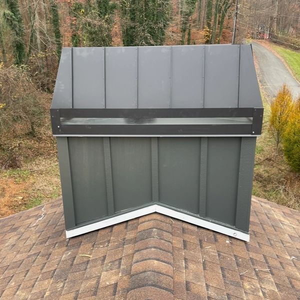 Gray metal vent on a rooftop in a wooded area.