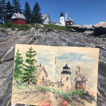Hand holds a watercolor sketch of a lighthouse matching the real scene behind it.
