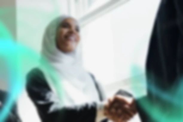Two people shaking hands in a bright setting, one wearing a hijab.