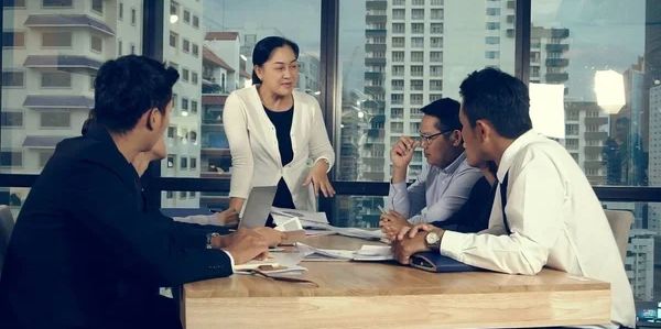 A businesswoman leads a meeting with three male colleagues in a modern office.