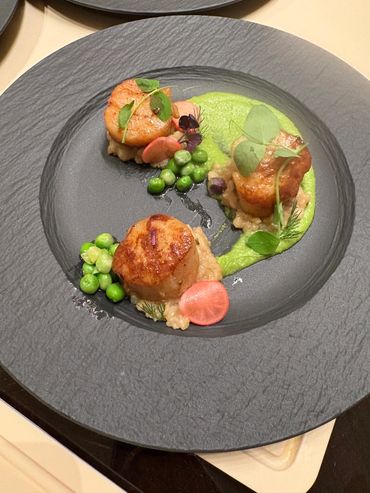 Seared scallops plated with green peas and garnish on a textured black plate.