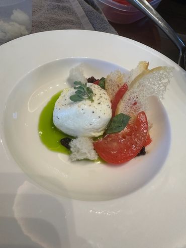 Gourmet dish with burrata, tomato, herbs, and crisp bread on a white plate.