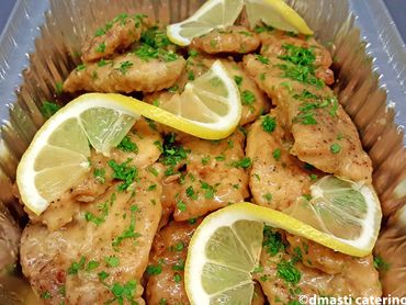 Fried chicken tenders garnished with lemon slices and chopped herbs in a tray.