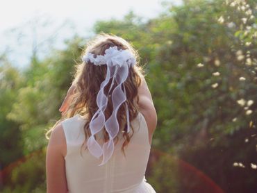 Woman with curly hair wearing a white dress and veil outdoors.