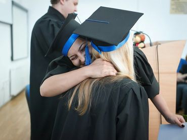 Two graduates in caps and gowns embrace joyfully during ceremony.