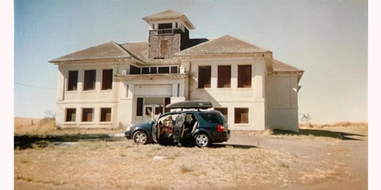 Old abandoned building with a parked car in front under clear sky.
