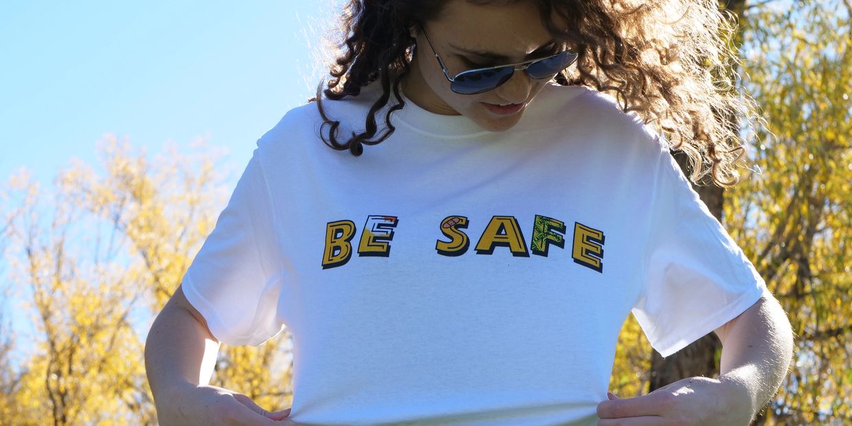 Woman wearing a white T-shirt with 'BE SAFE' text outdoors.
