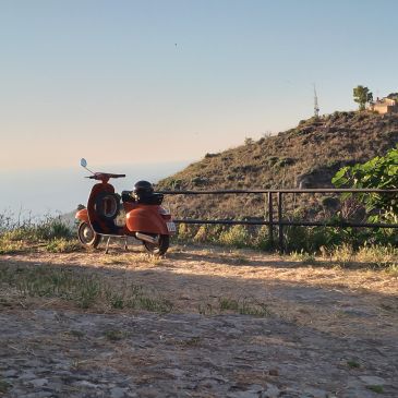 Orange scooter parked on a scenic hilltop with a clear sky.