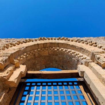 Ancient stone archway with wooden beam and metal gate against clear blue sky.