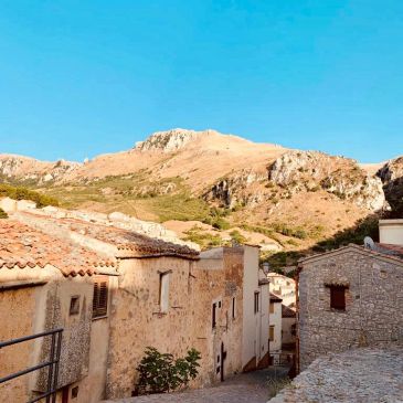 Sunny village street with stone houses and a mountain backdrop.