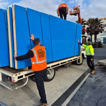 Workers unload large blue panels from a truck.