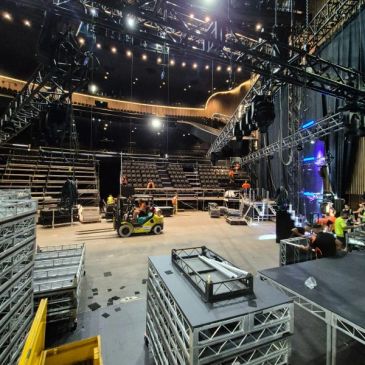 Crew setting up stage and seating for an event in a large indoor venue.