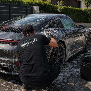 A man washing a black sports car covered in soap suds.