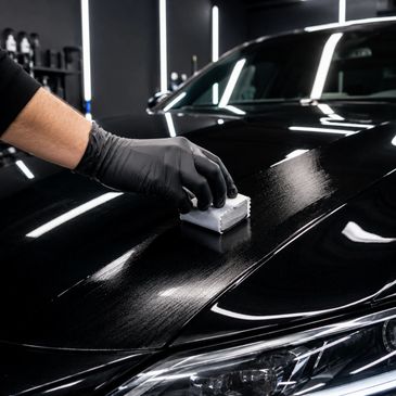 Person applying a protective coating on a sleek black car hood with a sponge.