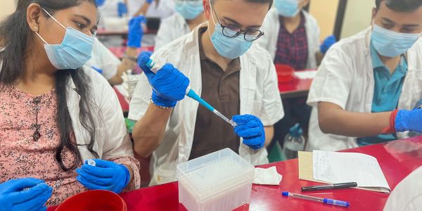 Students in lab coats and masks working with pipettes in a laboratory.
