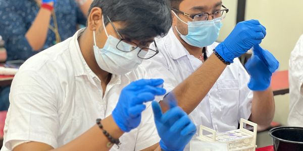 Two scientists in masks and gloves handling samples in a lab.