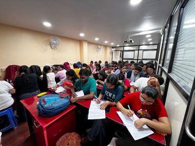 A crowded classroom with students focused on writing.