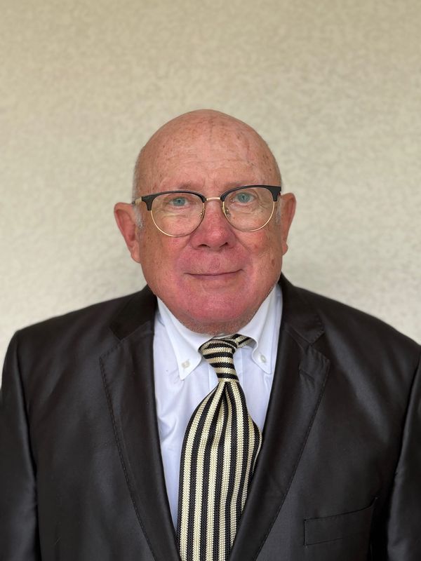 Elderly man in glasses and suit with striped tie smiling gently.