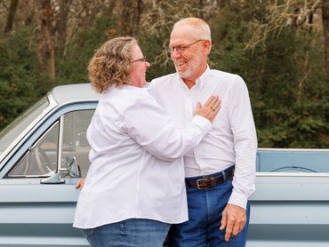 A happy mature couple embraces in front of a classic car outdoors.