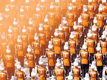 A large group of marching band members in orange uniforms with white hats.