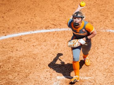 Softball pitcher in action mid-throw on the mound.